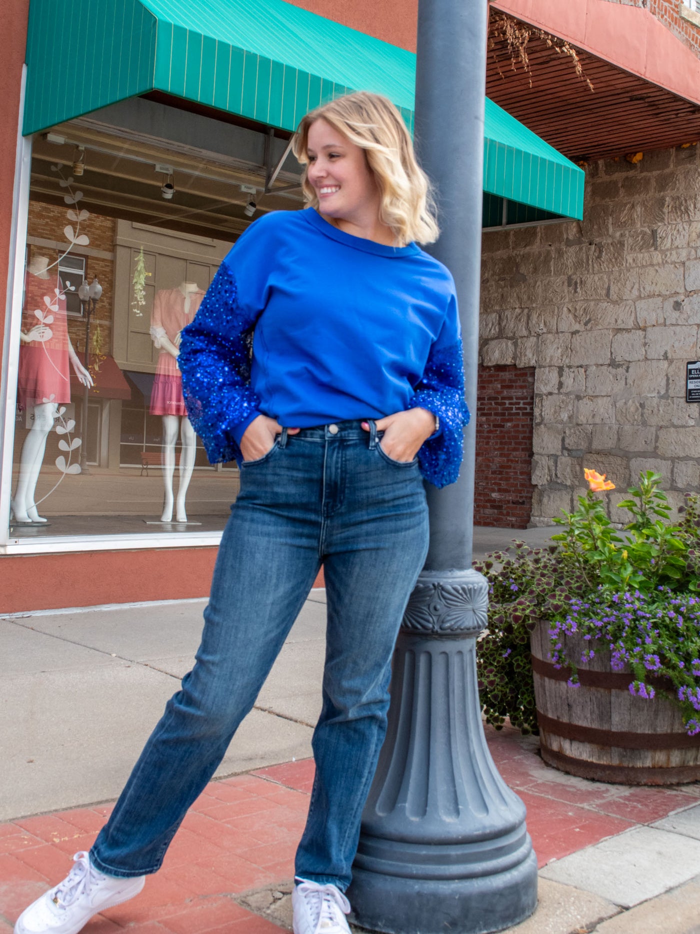 A model wearing a pair of straight leg high waisted jeans. She has them paired with a royal blue sweatshirt and white sneakers.