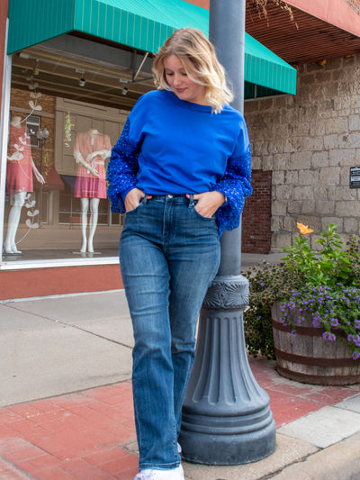 A model wearing a pair of straight leg high waisted jeans. She has them paired with a royal blue sweatshirt and white sneakers.