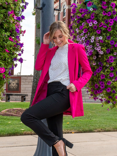 A model wearing a hot pink blazer. The model has it paired with a white polkadot top underneath and with a pair of black trousers.
