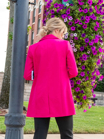 A model wearing a hot pink blazer. The model has it paired with a white polkadot top underneath and with a pair of black trousers.