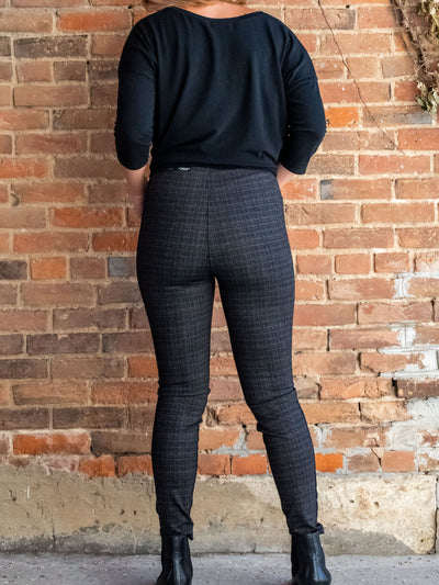 A model wearing a pair of plaid leggings with seam details. The model has them paired with a black v-neck top and black booties.