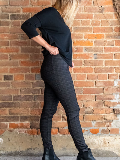 A model wearing a pair of plaid leggings with seam details. The model has them paired with a black v-neck top and black booties.