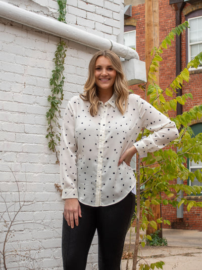 A model wearing a white button down blouse with polka dots. The model has it paired with pleather pants.