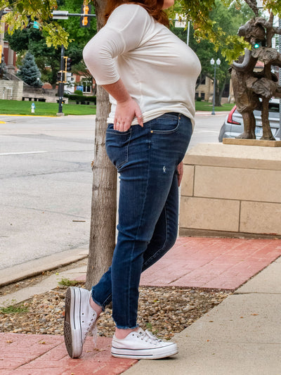 A model wearing a pair of medium wash skinny jeans with minimal distressing. The model paired it with a white v-neck top and white sneakers.