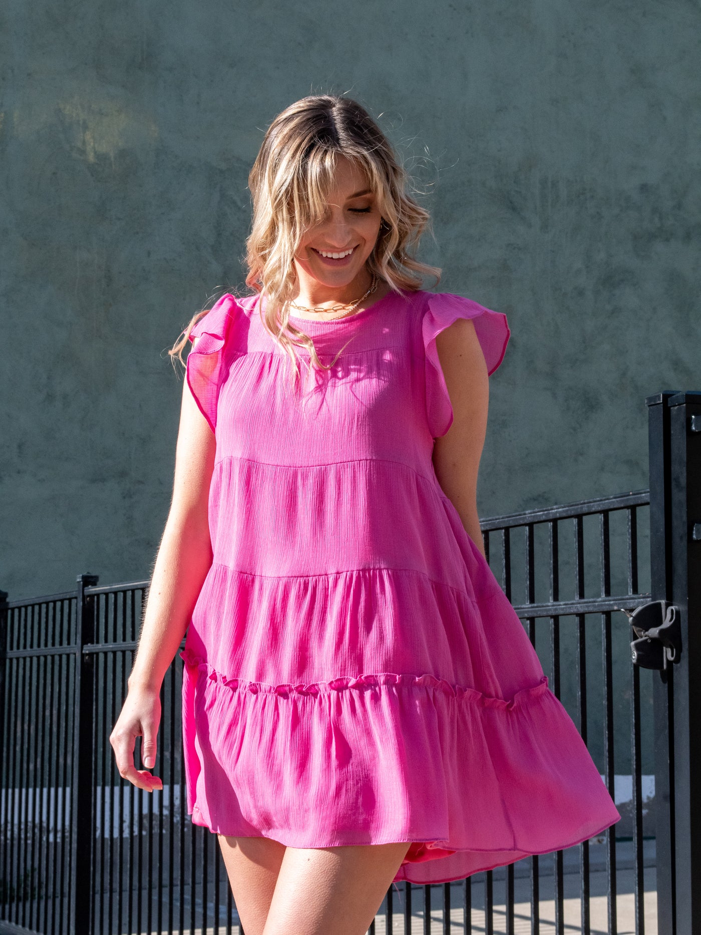 A model wearing a pink ruffled tiered lined mini dress. She has it on with white sneakers.