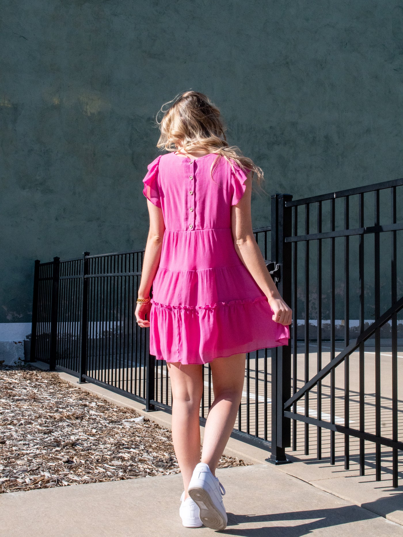 A model wearing a pink ruffled tiered lined mini dress. She has it on with white sneakers.
