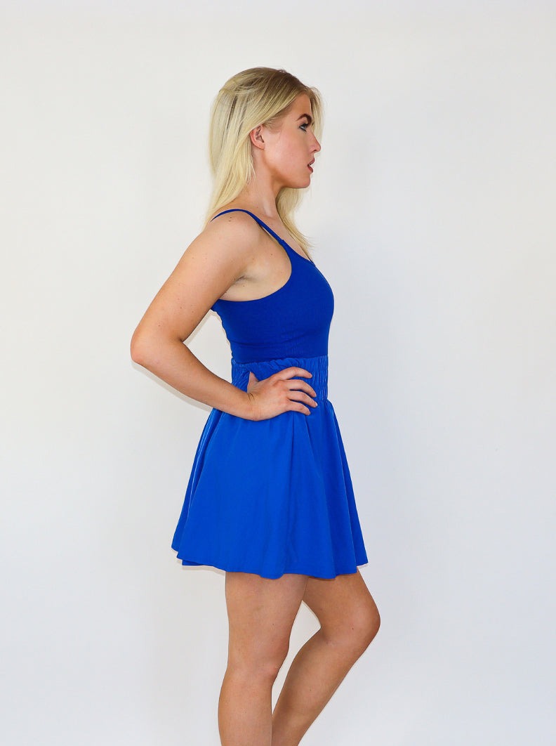 Model is wearing an electric blue mini athletic tennis dress with ruching at the waist and a flowey skirt. 