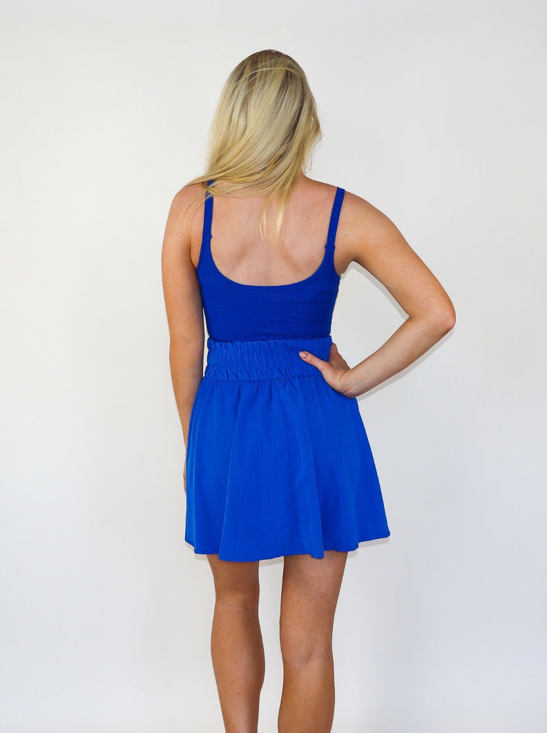 Model is wearing an electric blue mini athletic tennis dress with ruching at the waist and a flowey skirt. 