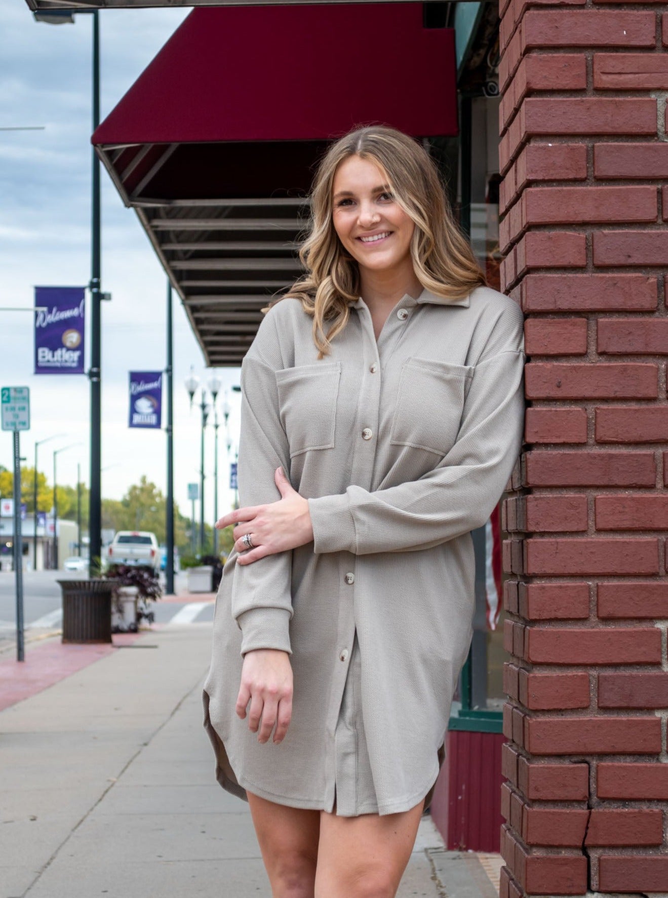A model wearing an oatmilk colored button down dress. The model has it paired with black booties.