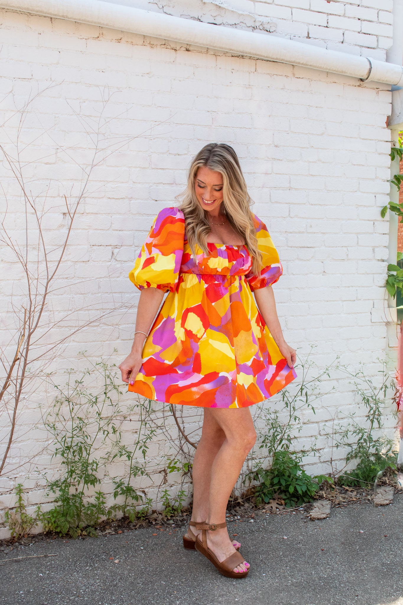 A model wearing a pink, orange, purple, and yellow empire waist mini dress with puff sleeves. She has paired it with brown platform sandals.
