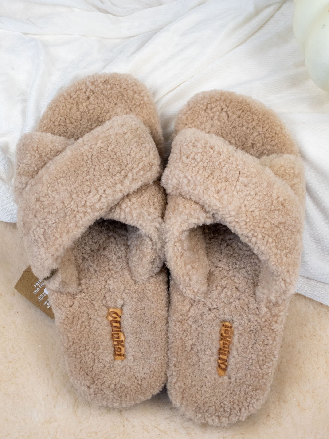 A pair of beige shearing slippers with a criss cross design and rubber base.
