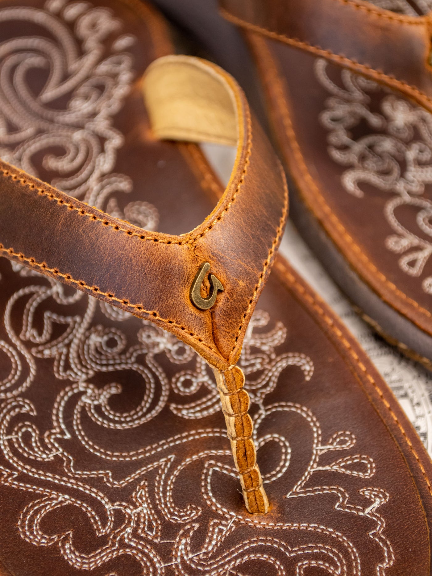 A brown leather sandal with stitching details and between the toe strap.