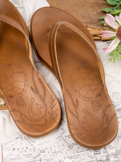 A light brown leather sandal with stitching and between the toe strap.