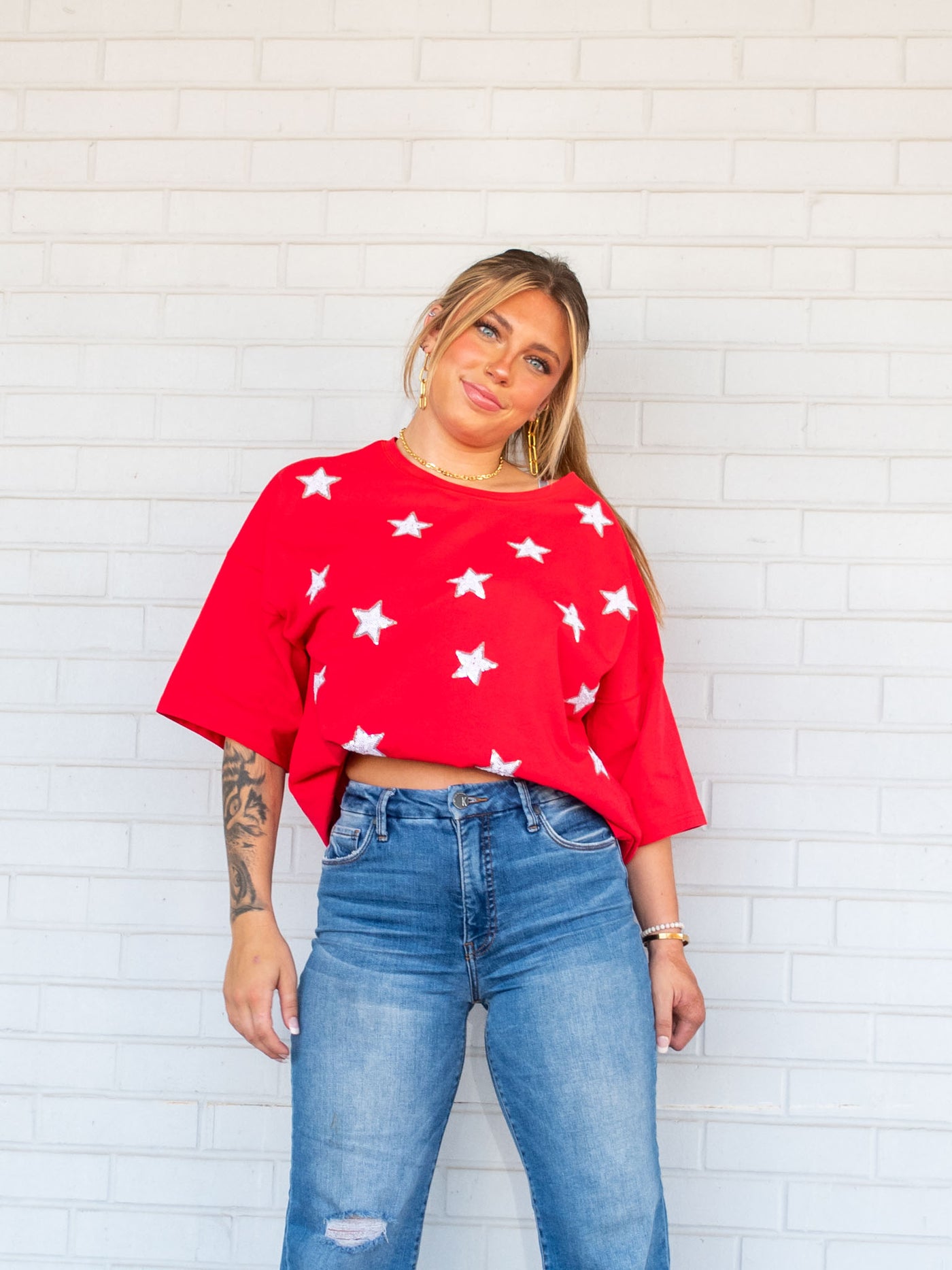 A model wearing an oversized, red tee with white sequin stars all over it. She has it paired with a light wash jean.