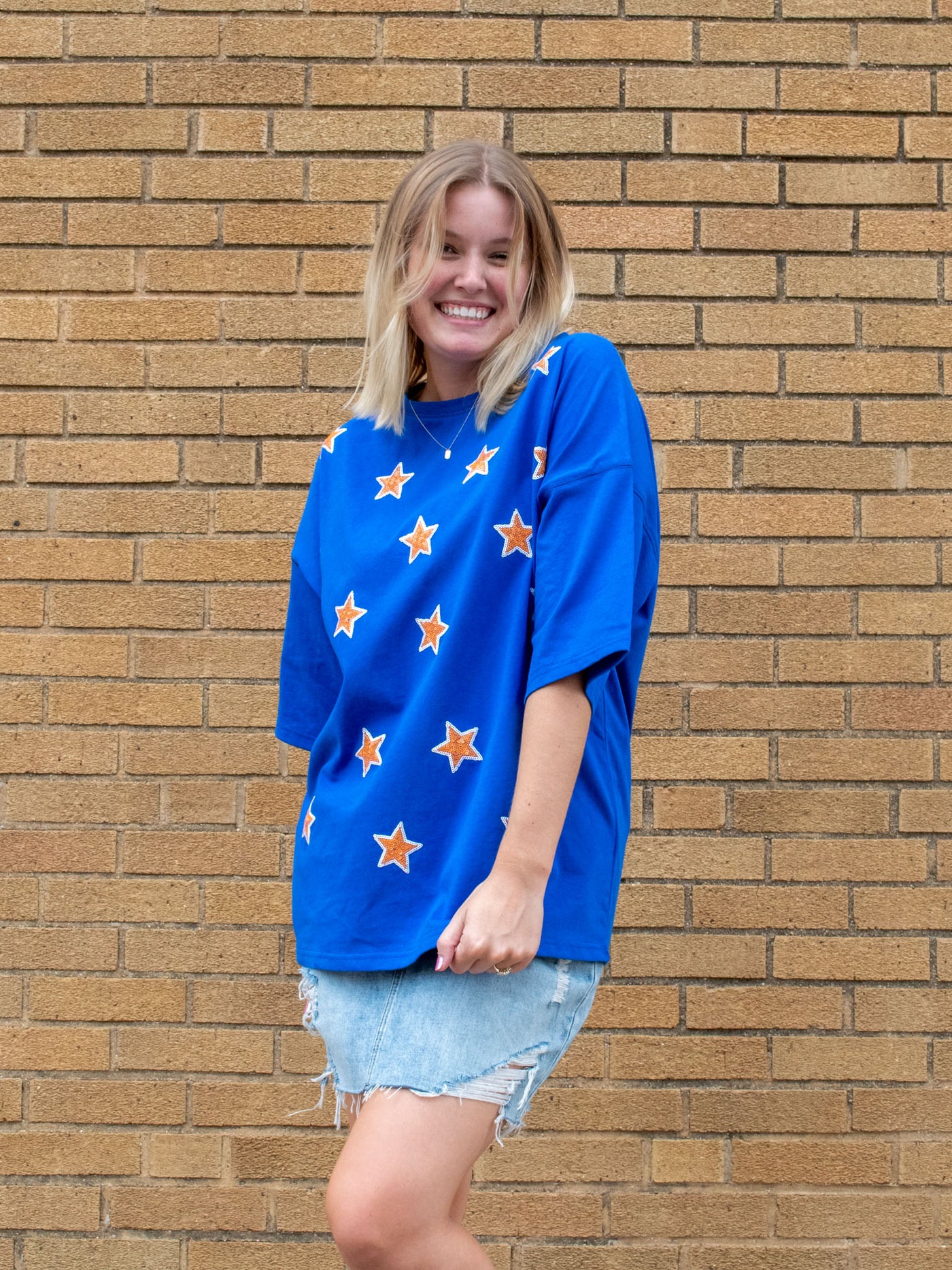 A model wearing a blue oversized tee with gold and white sparkly stars on it. The model has it paired with a light washed denim skirt.