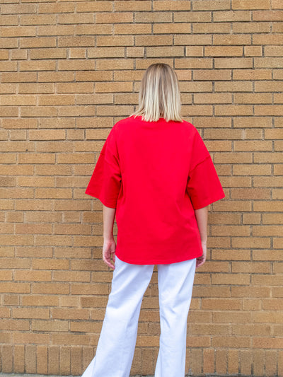 A model wearing a red oversized tee with white sparkly stars on it. The model has it paired with a white jean.
