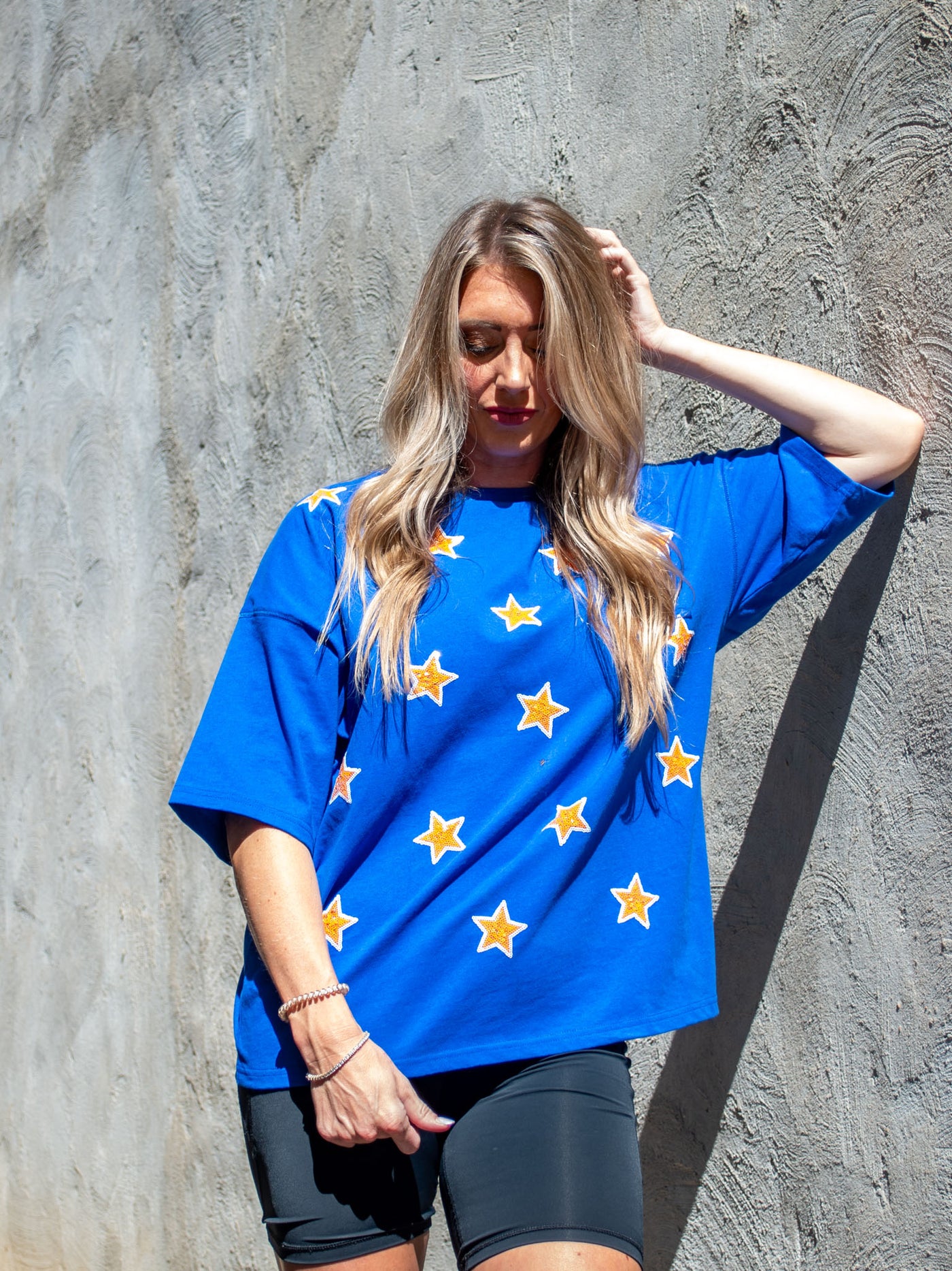 A model wearing an oversize blue tee with gold sequin stars on it. She has it paired with black biker shorts.