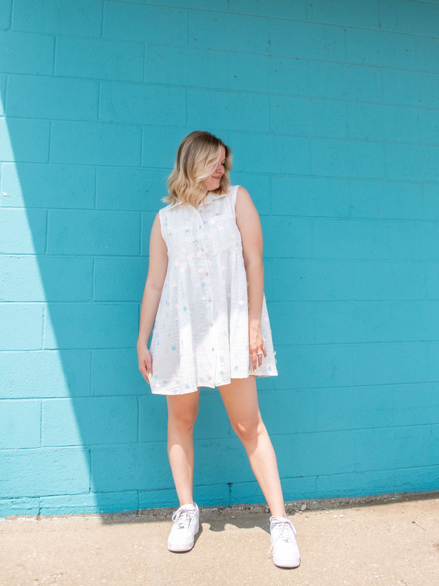 A model wearing a white sequin button down dress with white sneakers. 