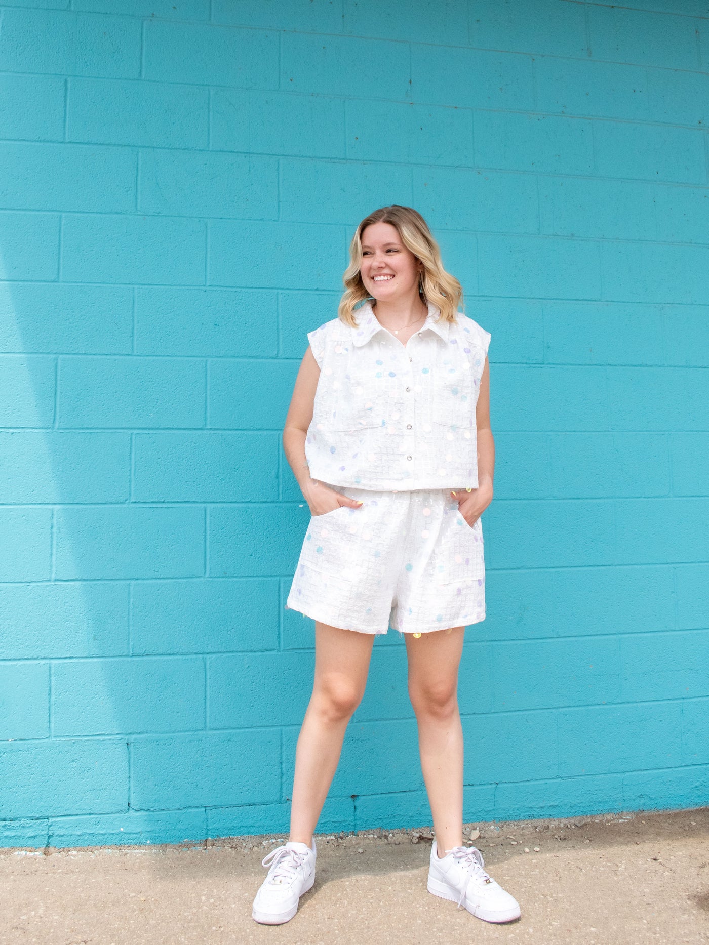 A model wearing a checker palette collar top with sequins and buttons down the front. She has it paired with matching shorts and white sneakers. 