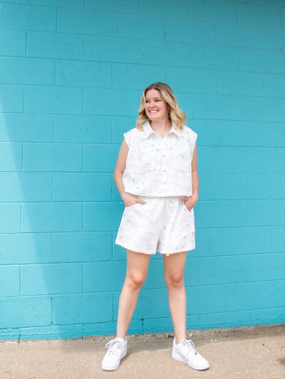 A model wearing a checker palette collar top with sequins and buttons down the front. She has it paired with matching shorts and white sneakers. 