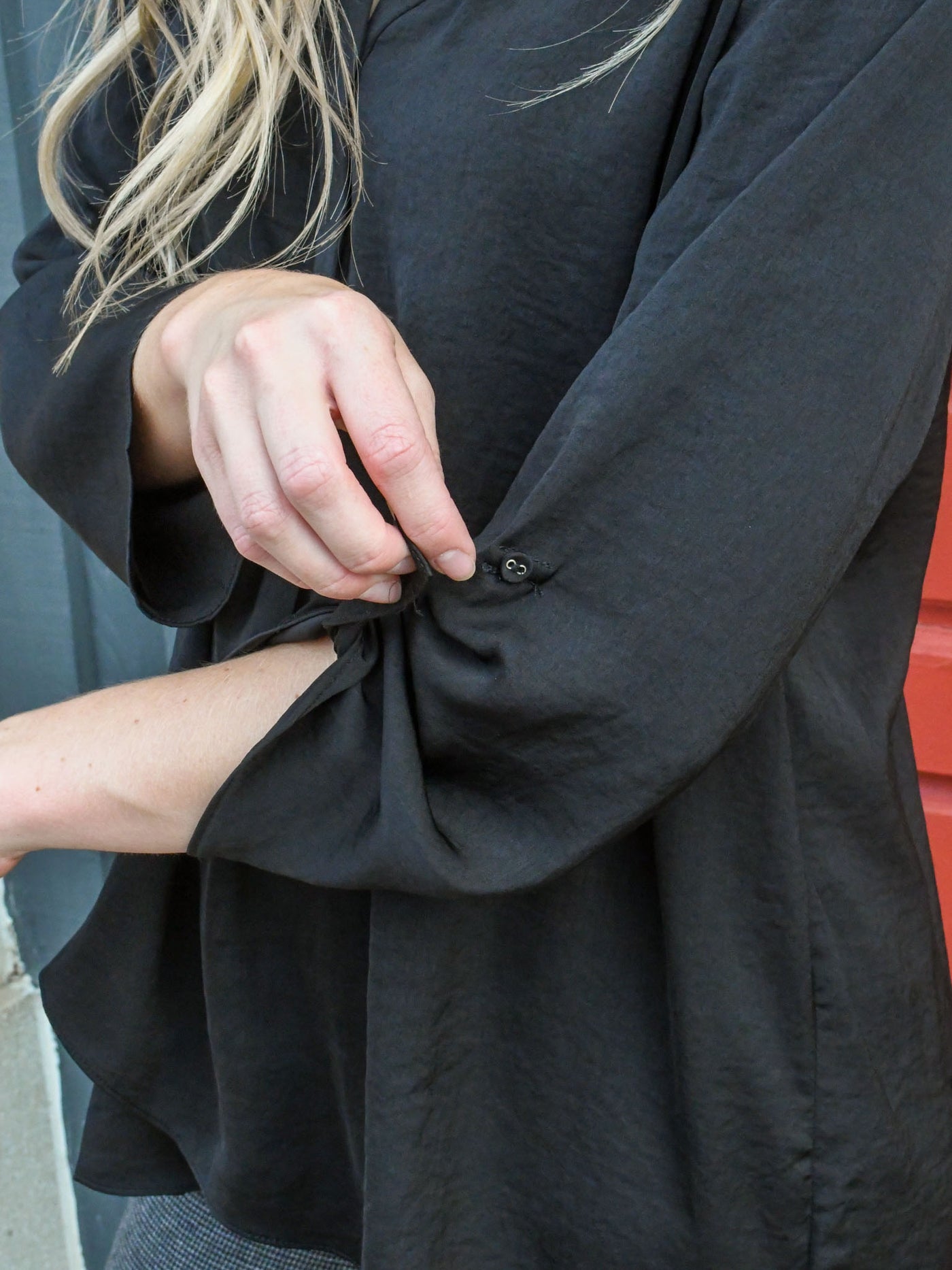 A model wearing a black airflow top with a v-neckline and adjustable sleeves. The model has it paired with a wide leg trouser.