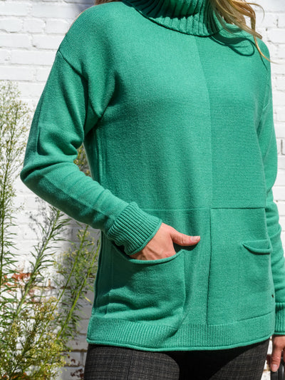 A model wearing a green turtleneck sweater with seam details. The model has it paired with a black and brown plaid legging.