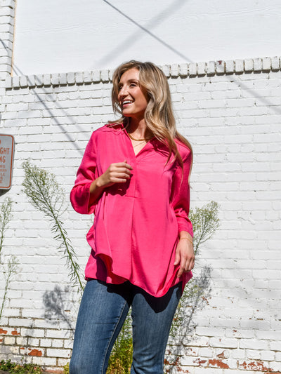 A model wearing a hot pink airflow blouse pinned up sleeves and a v-neckline with collar. She has it paired with dark wash jeans.