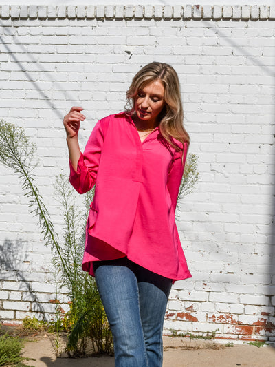 A model wearing a hot pink airflow blouse pinned up sleeves and a v-neckline with collar. She has it paired with dark wash jeans.