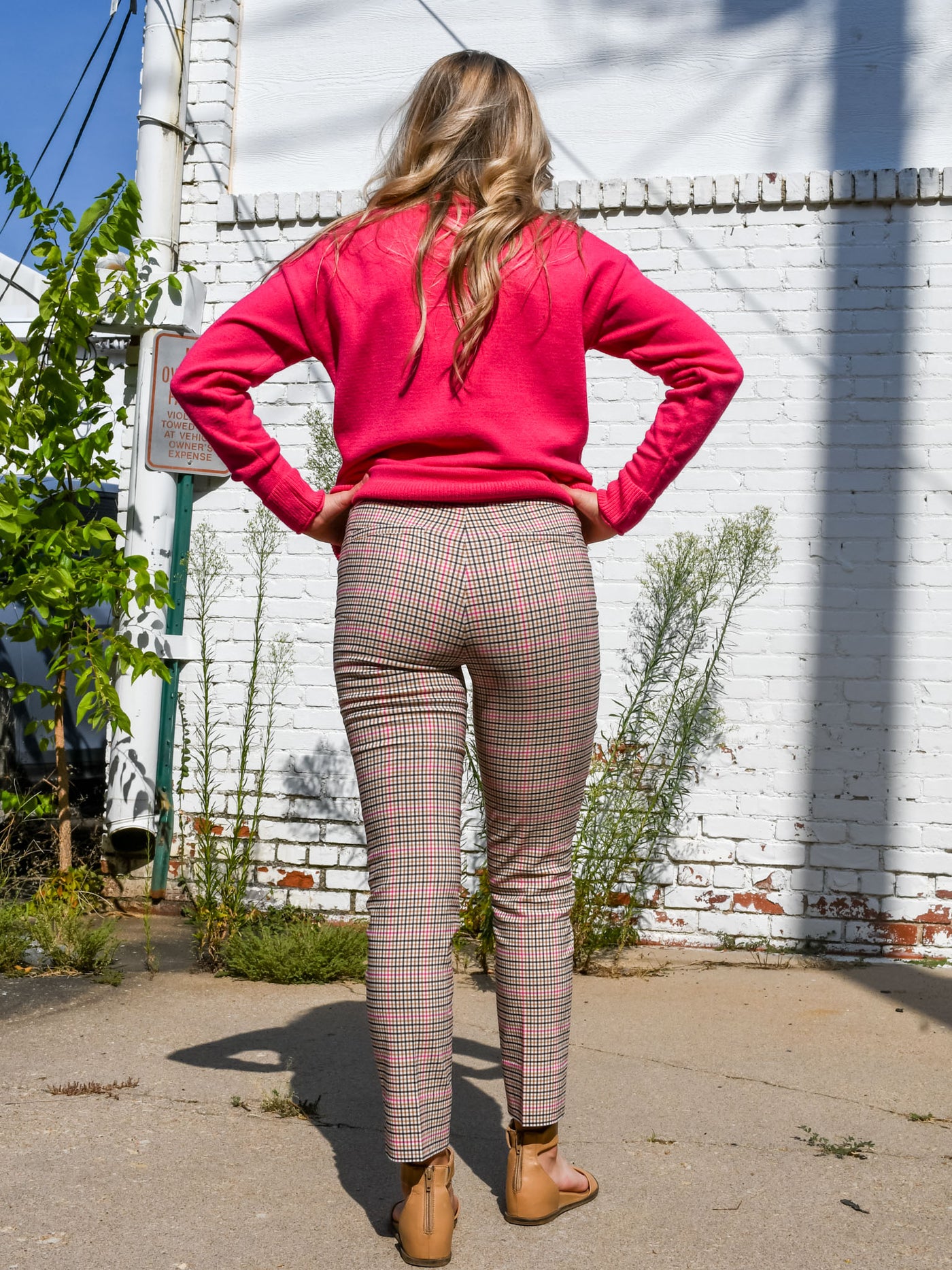A model wearing a pair of pink plaid ankle length dress pants. The model has them paired with a pink turtleneck sweater, a beige purse and brown sandals.