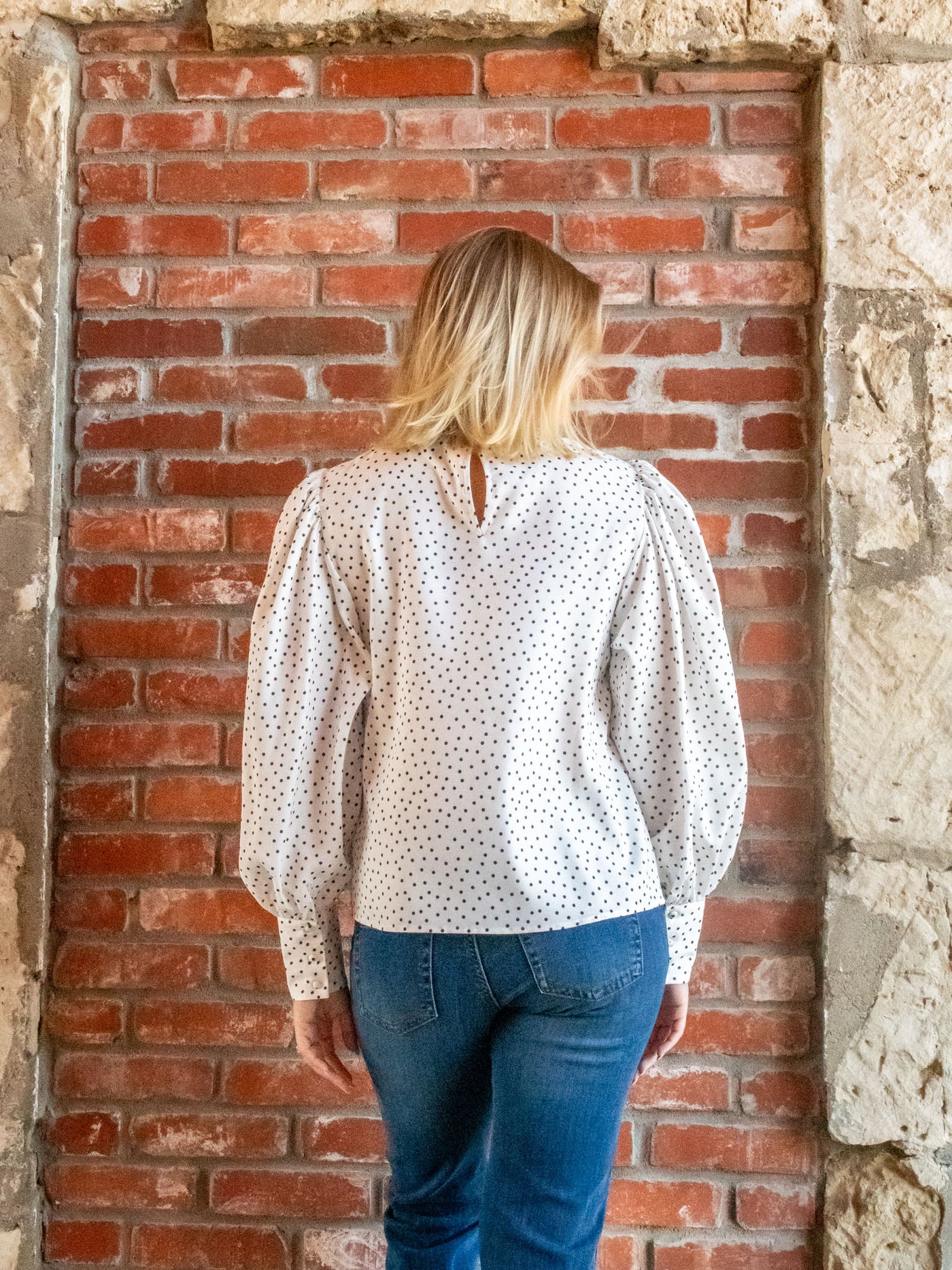 A model wearing a white blouse with puff sleeves and black polka dots. The model is wearing it with a pair of medium washed jeans.