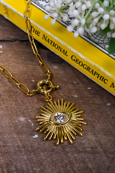 A gold chain link necklace with a sun pendant and a stone center.
