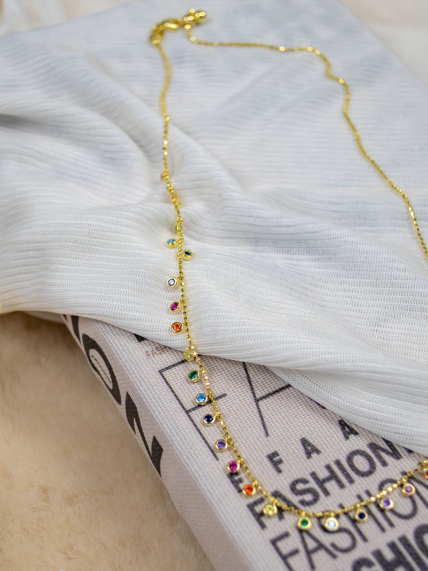A gold choker necklace with many colorful CZ stones dangling off the front.