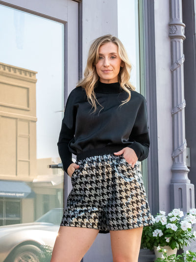 A model wearing a pair of black and silver houndstooth sequin shorts. She has them paired with a black satin top.