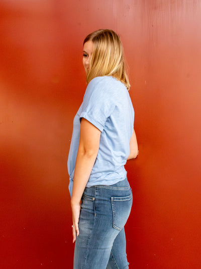 A light blue t-shirt with cuffed sleeves and a tie front detail. The model has it paired with a pair of light wash jeans.