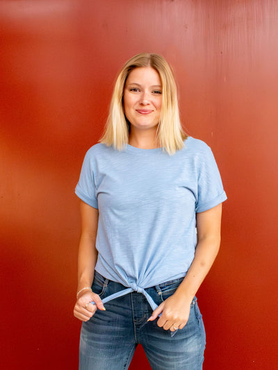 A light blue t-shirt with cuffed sleeves and a tie front detail. The model has it paired with a pair of light wash jeans.