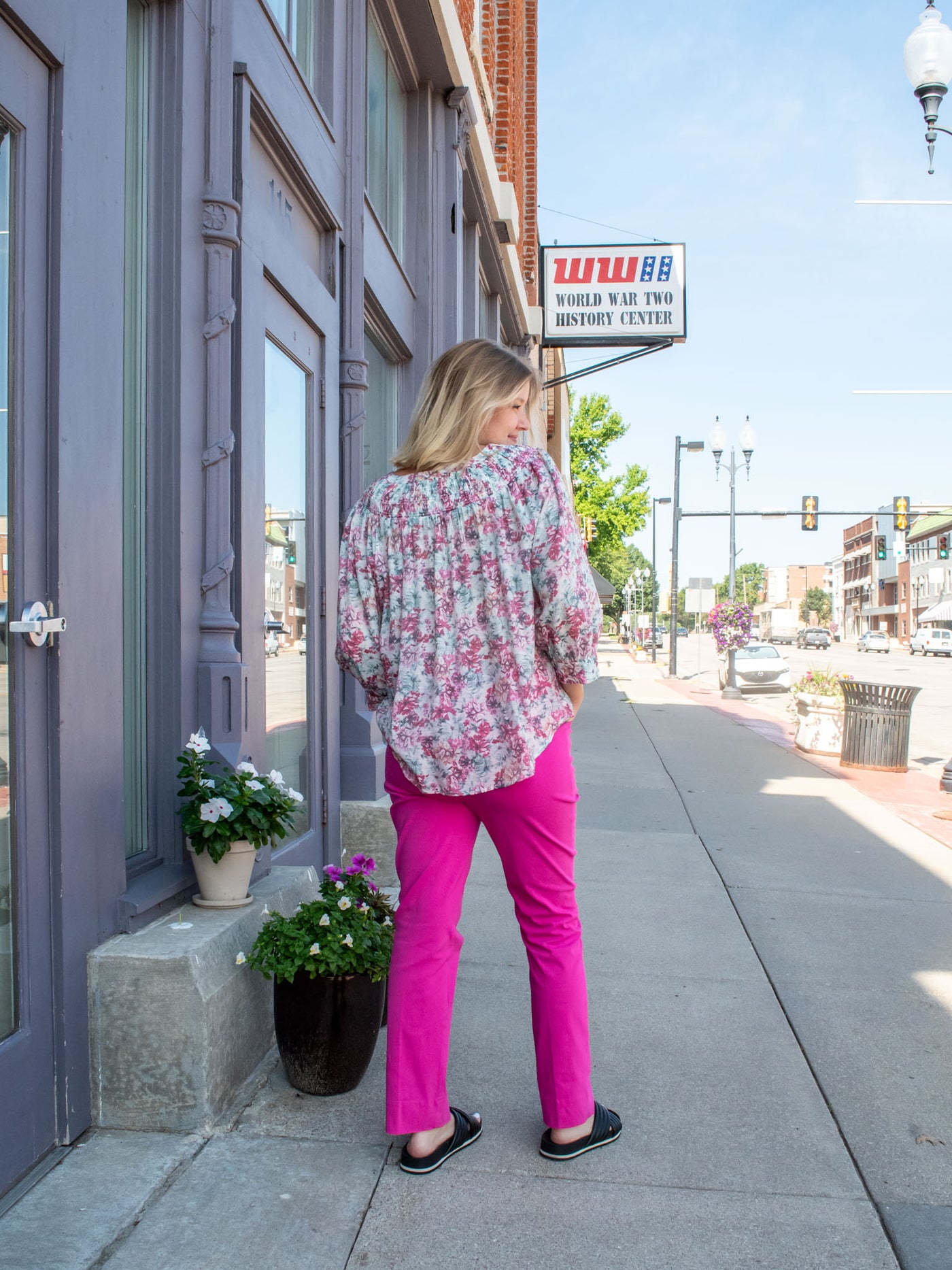 A model wearing a white blouse with a pink and green floral pattern on it. The model has it paired with a hot pink pant and black sandals.