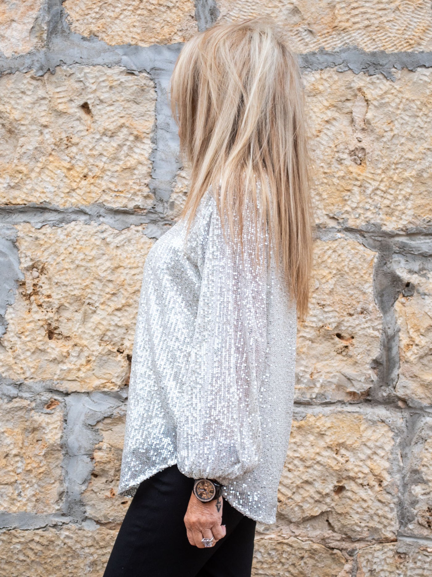 A model wearing a silver all over sequin top with a sleeve cuff and balloon sleeve. The model has it paired with a pair of black skinny jeans.