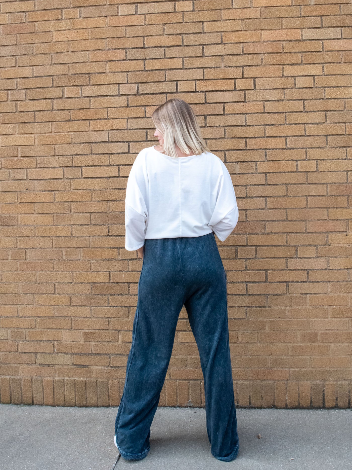 A model wearing a high waisted, drawstring navy sweatpants. She has them paired with a white top and white sneakers.