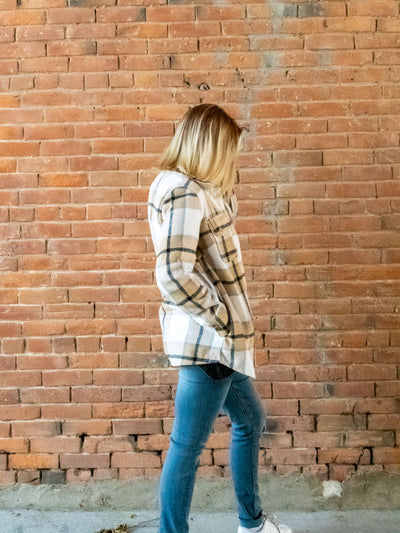 A model wearing a light brown plaid shacket with a button closure. She has it paired with a pair of light wash jeans.