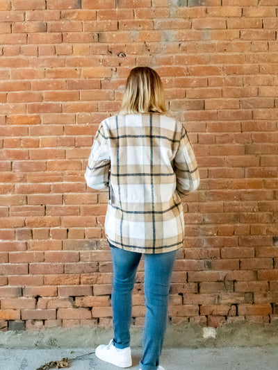A model wearing a light brown plaid shacket with a button closure. She has it paired with a pair of light wash jeans and white sneakers.