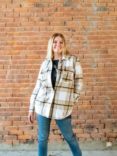 A model wearing a light brown plaid shacket with a button closure. She has it paired with a gray top underneath and a pair of light wash jeans.