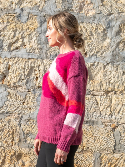 A model wearing a pink, orange, and purple printed crewneck sweater. The model has it paired with black slacks.