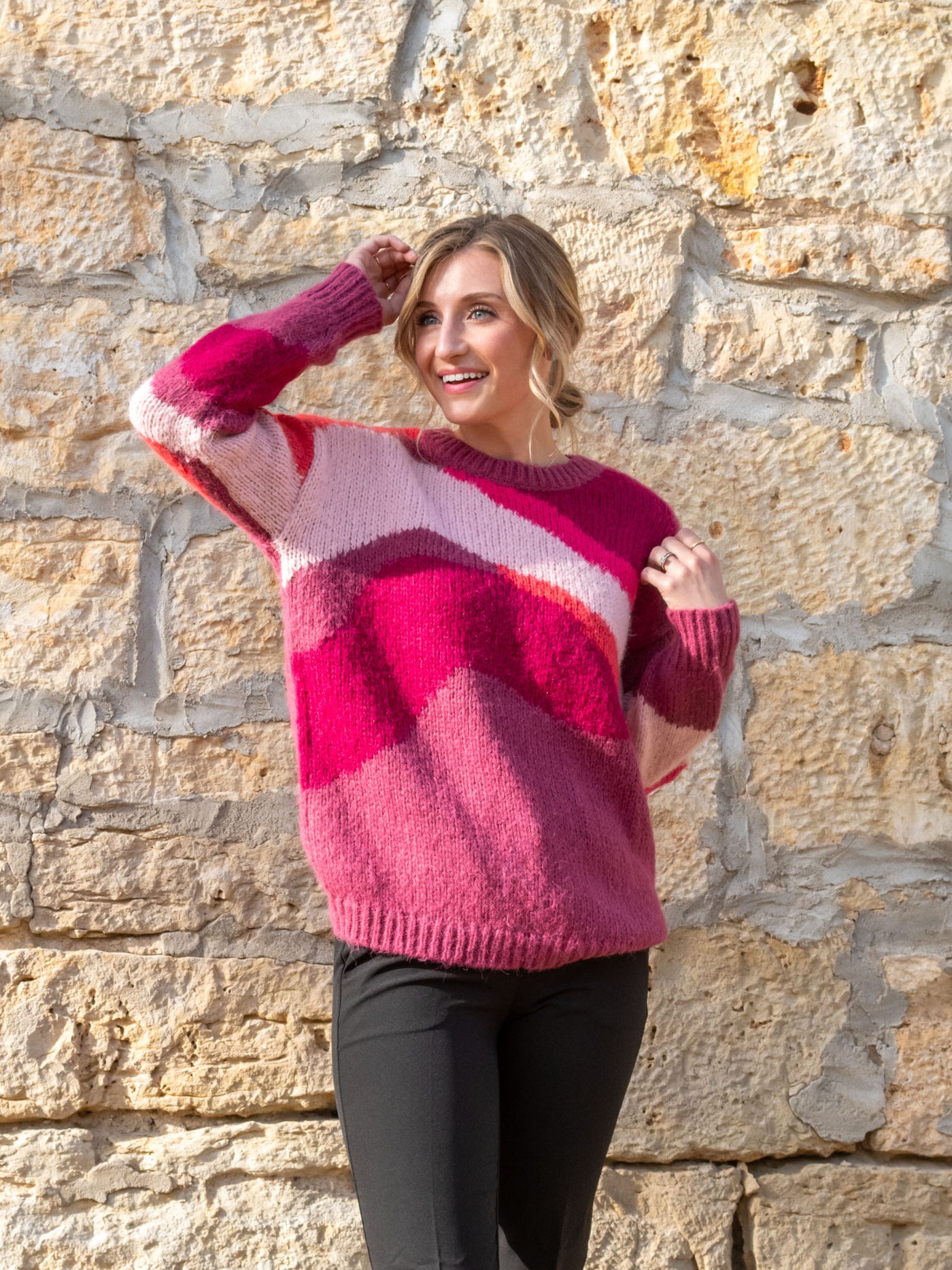 A model wearing a pink, orange, and purple printed crewneck sweater. The model has it paired with black slacks.