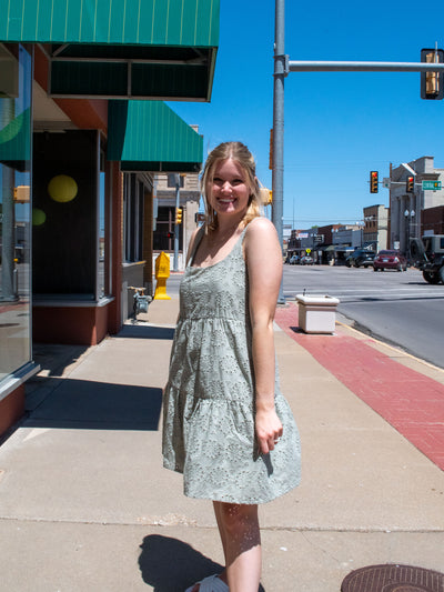 A model wearing a green short eyelet embroidery dress with side pockets. She has it on with white shoes.