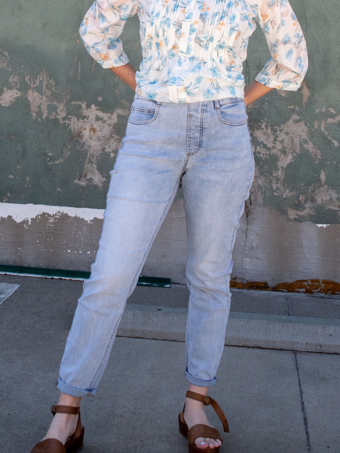 A model wearing a pair of light wash pull on leggings with a floral blouse and brown platform sandals.