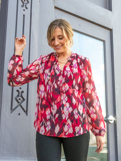 A model wearing a pink, red and purple multicolored printed blouse. The model has it paired with a black trouser.