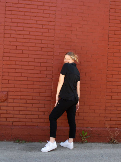 A model wearing a pair of black pull on activewear technical pants with a black v neck top and white sneakers.