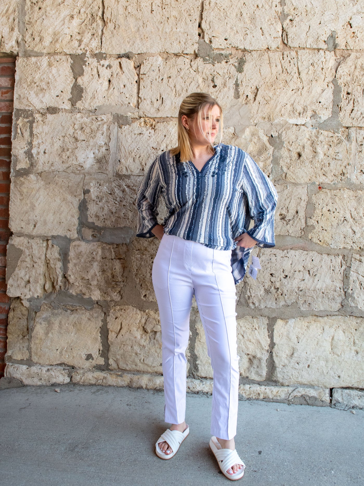 A model wearing a pair of white front seam pull-on pants with a blue striped top and white slides.