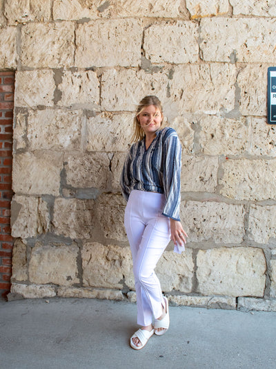 A model wearing a pair of white front seam pull-on pants with a blue striped top and white slides.
