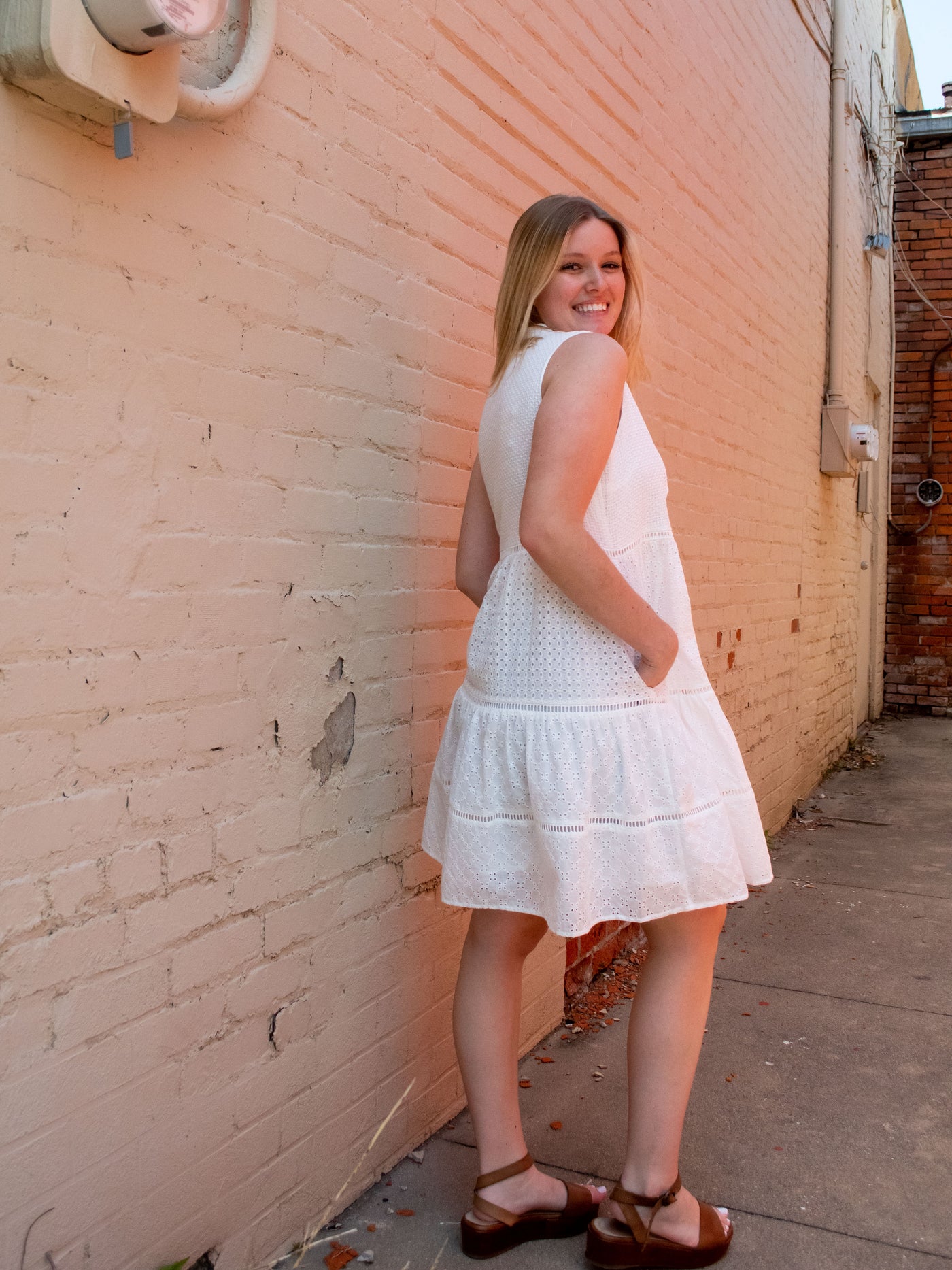 A model wearing a white empire waist eyelet dress and brown platform sandals.